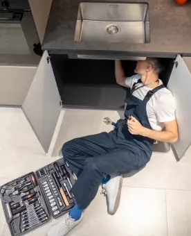 A man performing a repair under a kitchen sink.