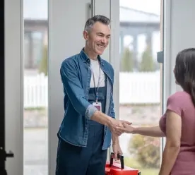 A man in overalls shaking hands with a woman after completing a quality repair job.